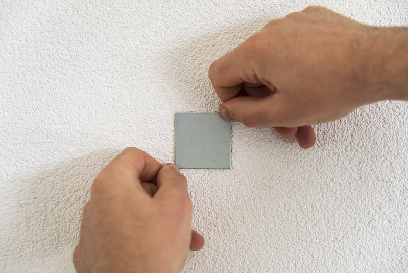 Twee handen pakken de kunststof strips vast om het metalen muurplaatje draaiend te verwijderen